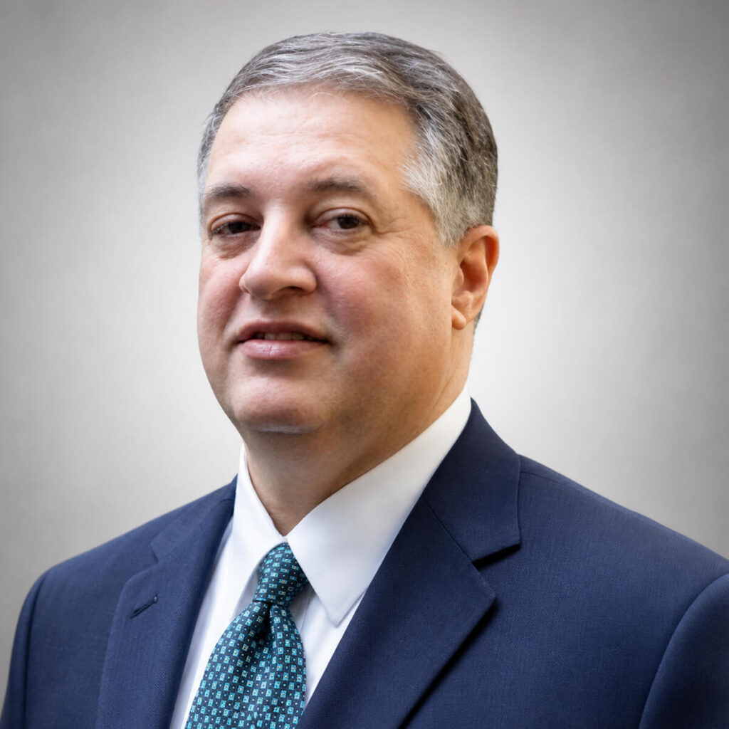 Head-and-shoulders portrait of a middle-aged man in a navy suit and teal patterned tie, looking at the camera.