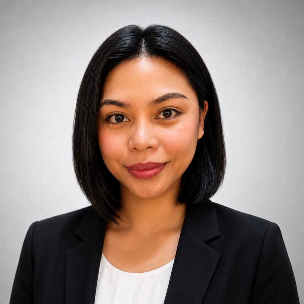 Professional headshot of a woman with shoulder-length black hair wearing a black blazer and white blouse, smiling at the camera against a neutral gray background