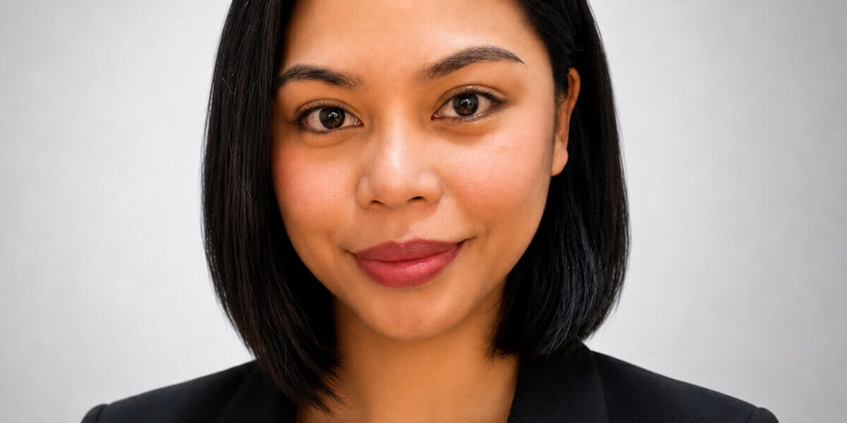 Kes-Yusay Professional headshot of a woman with shoulder-length black hair wearing a black blazer and white blouse, smiling at the camera against a neutral gray background