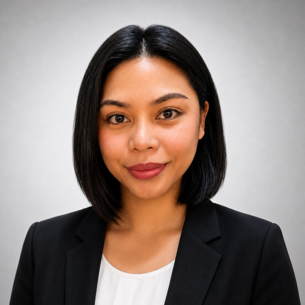 Professional headshot of a woman with shoulder-length black hair wearing a black blazer and white blouse, smiling at the camera against a neutral gray background