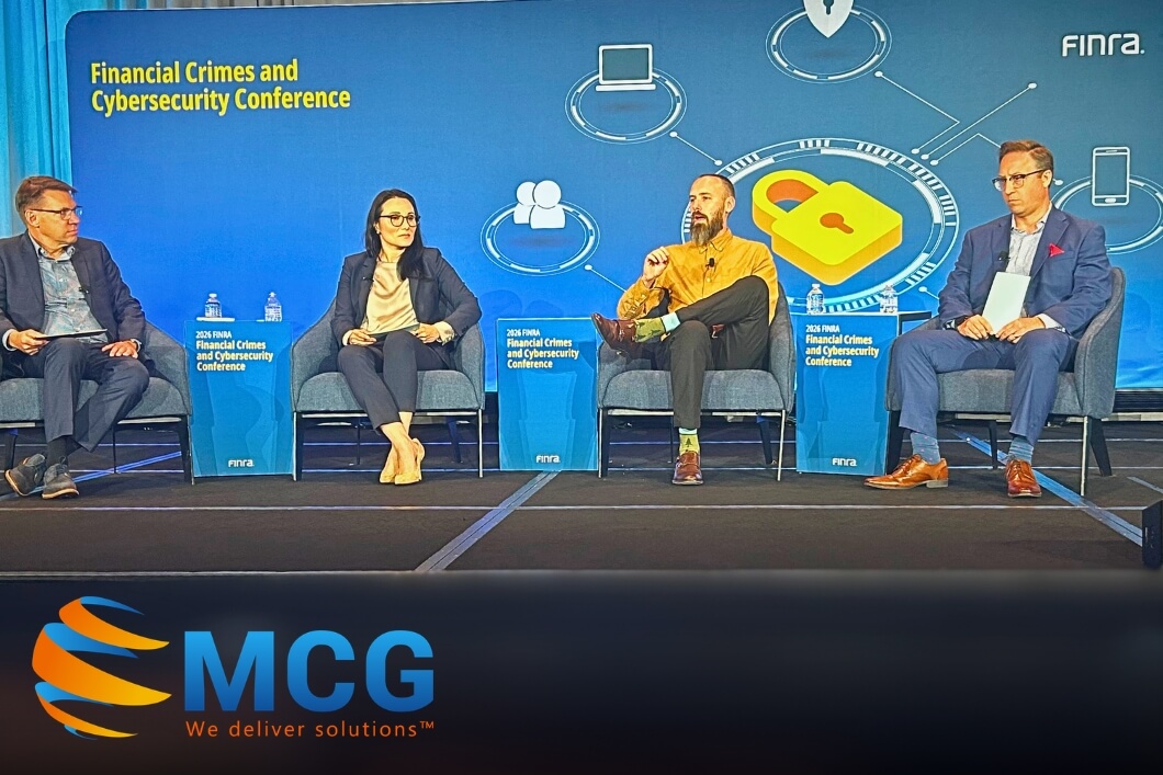 Panel discussion on stage at a Financial Crimes and Cybersecurity Conference with four speakers seated in blue chairs and a large blue backdrop featuring a lock icon and circuit graphics, MCG logo visible bottom left.